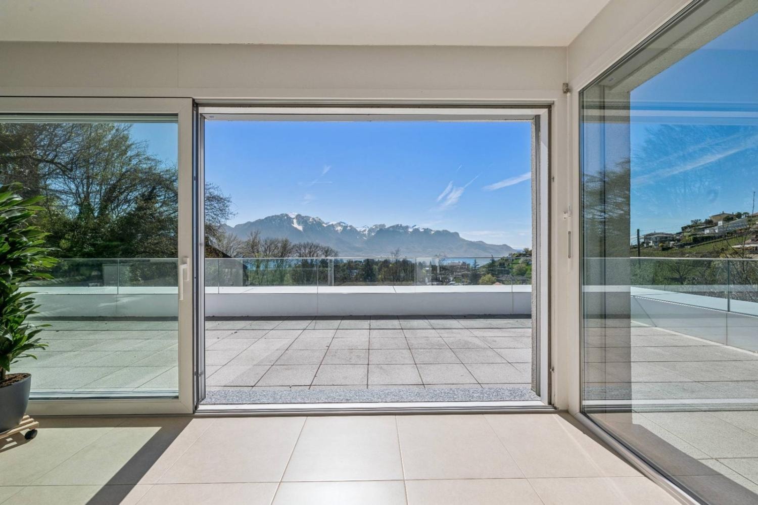 Floor-to-ceiling glass doors opening onto the panoramic terrace with Lake Geneva and Alpine views
