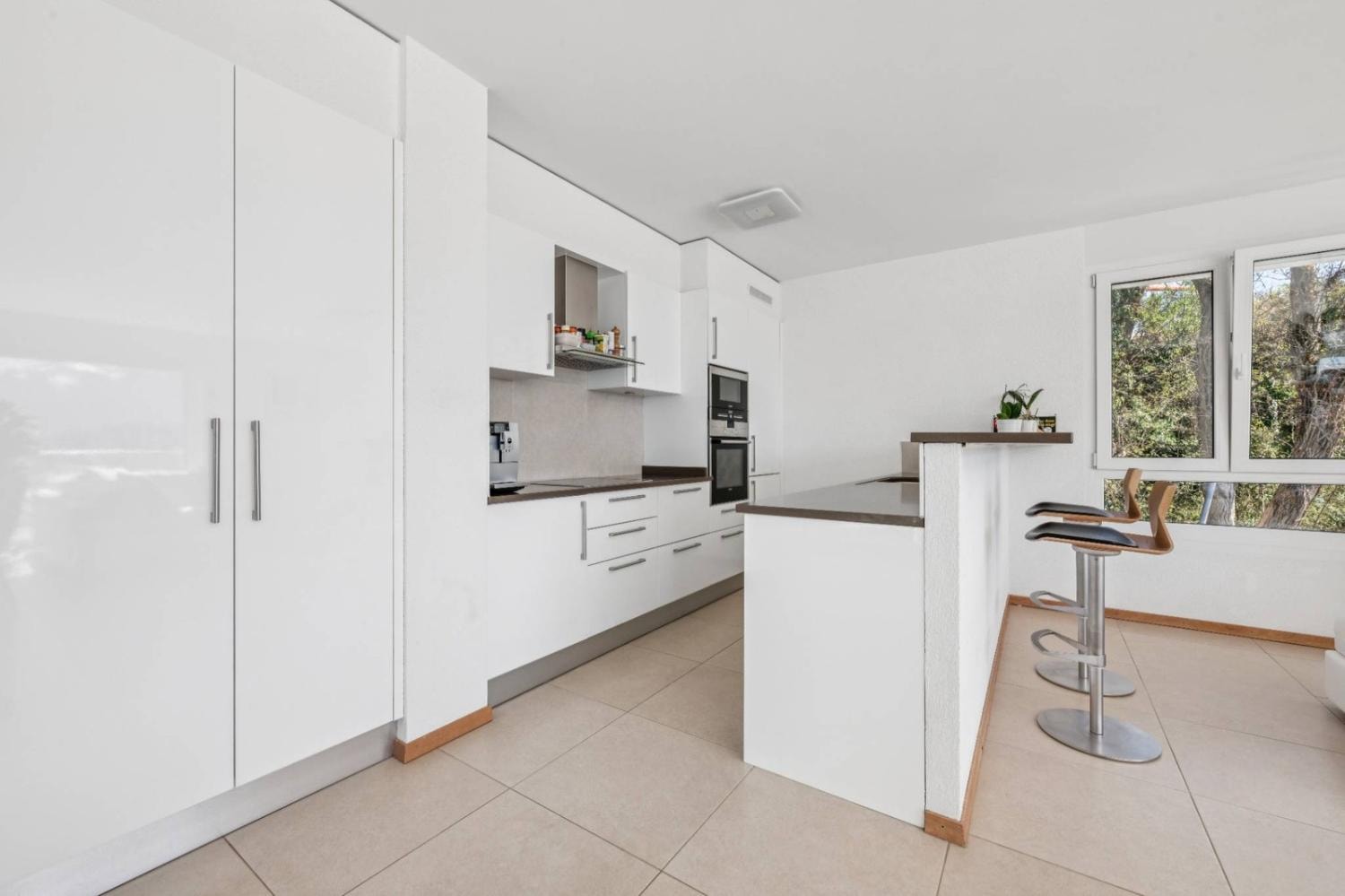 Modern white fitted kitchen with bar counter and garden view, Montreux duplex penthouse