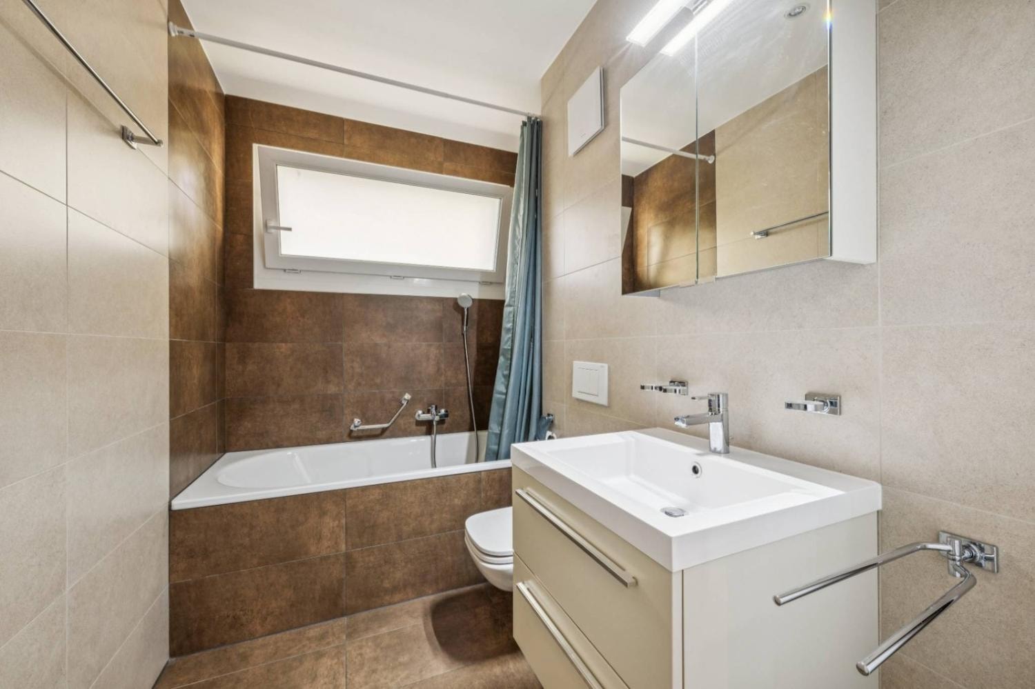 Bathroom with bathtub, brown stone tiling and vanity unit